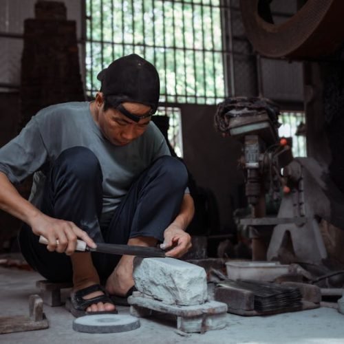 Adult man sharpening a knife on a stone in a traditional workshop setting. Indoor craft scene.
