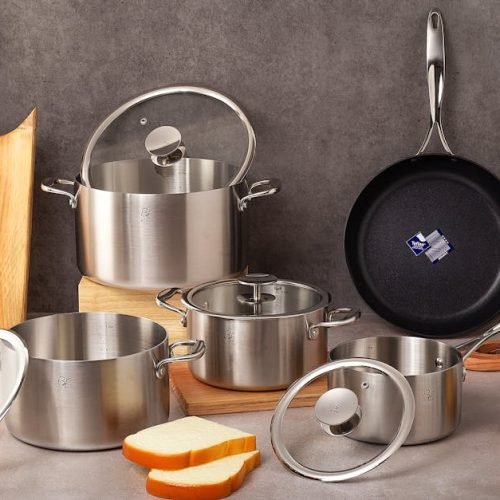 Premium stainless steel cookware set with wooden cutting board and vegetables.