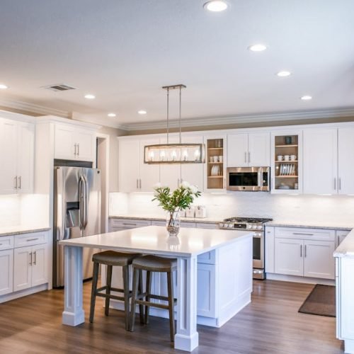 Elegant white kitchen featuring an island, modern appliances, and ample natural light.