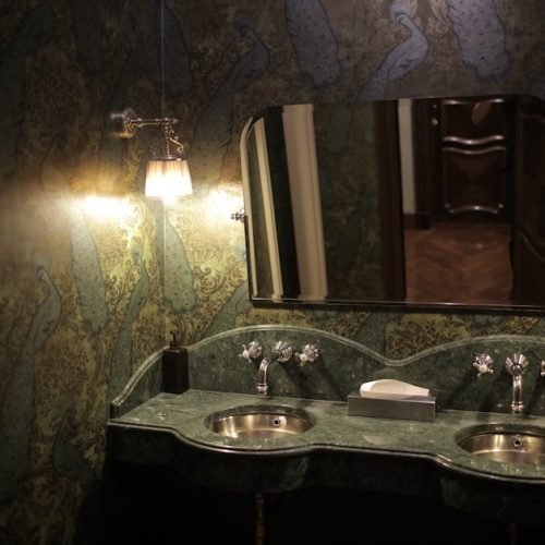 Luxurious bathroom featuring twin sinks with elegant green marble countertops and decorative wallpaper.